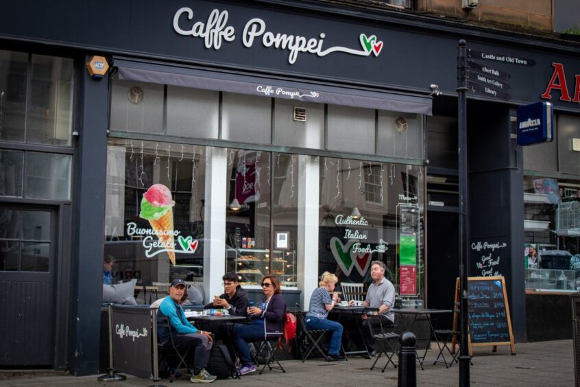 Diners sit outside the dark grey exterior of Caffe Pompei in Stirling city centre eating their food.