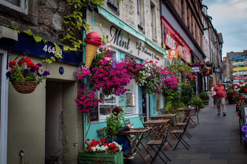 Cream and mint green exterior of Mint cafe and patisserie in Stirling, with wooden tables and chairs outside and a hanging baskets full of colourful flowers.