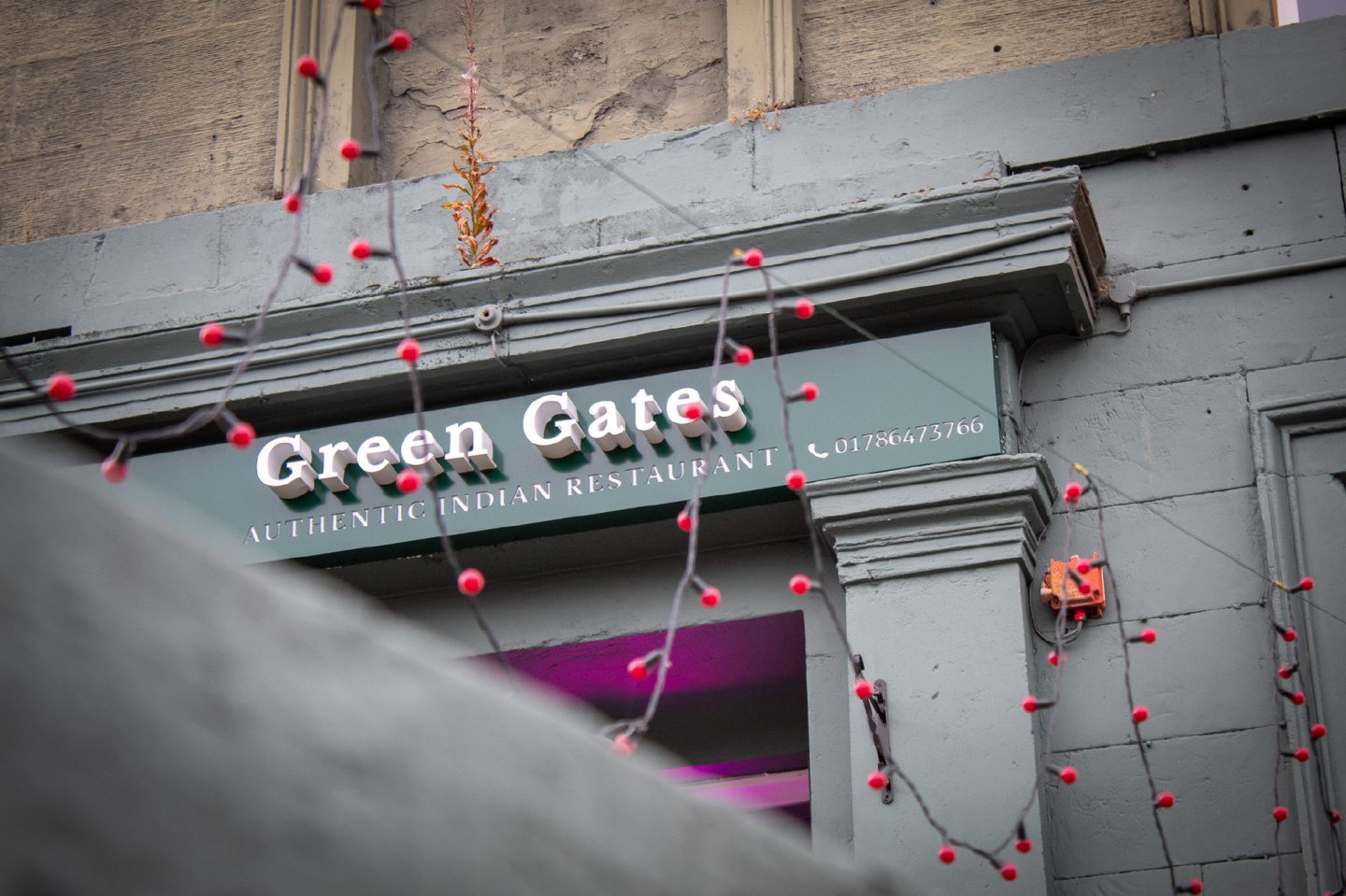 Close-up of exterior sign of Stirling Indian restaurant Green Gates, with red festoon lighting hanging outside