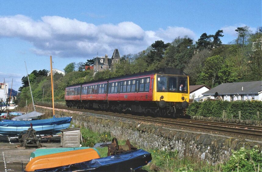 boats pulled up to a wall as a Dundee-Carnoustie train goes along a seaside track