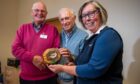 Two men handing wooden plaque to woman