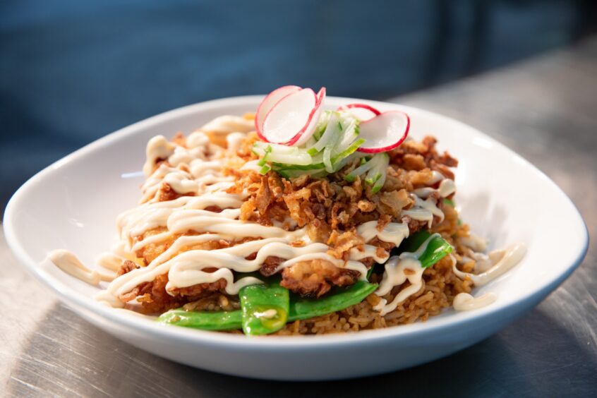 The finished dish: fried rice with greens, with golden crispy firied chicken, topped with honey soy sauce, sriracha, fried onions, Julienne cucumber and sliced radishes.