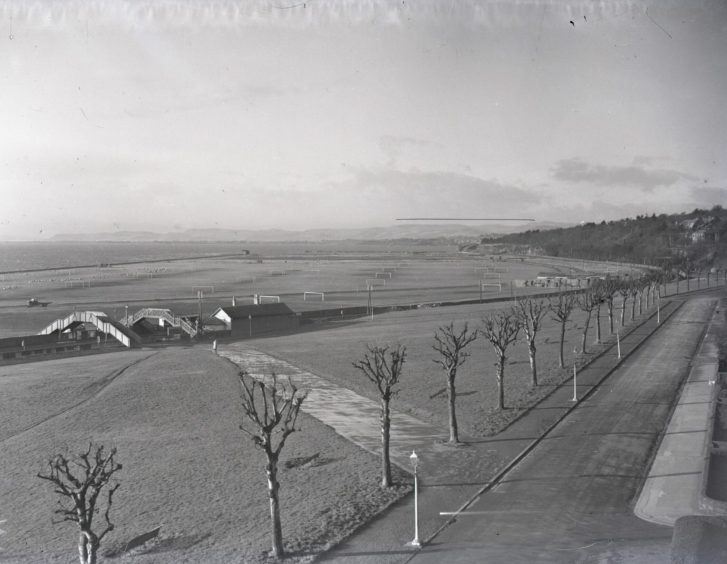 an aerial view show trees, football pitches and Magdalen Green Station in January 1951, with the River Tay visible in the distance.