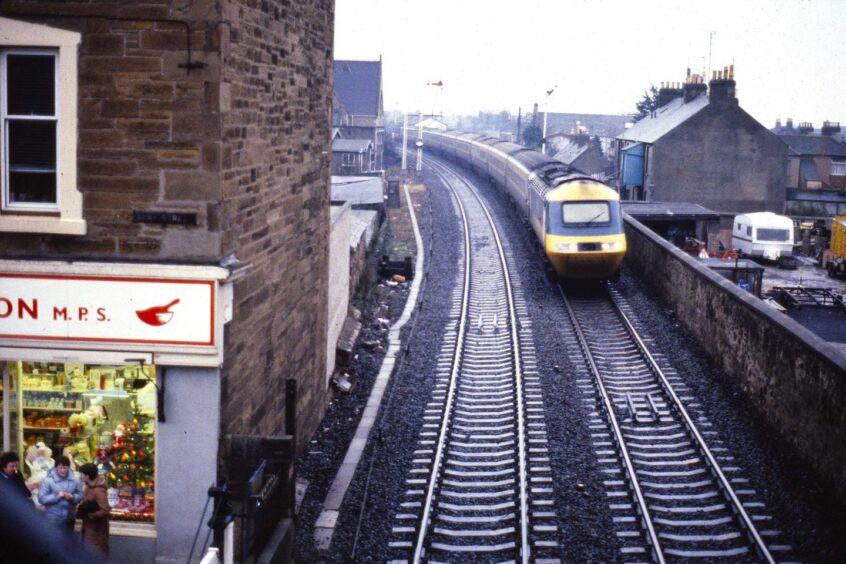 People stand outside a shop as InterCity 125 goes past the footbridge in Broughty Ferry