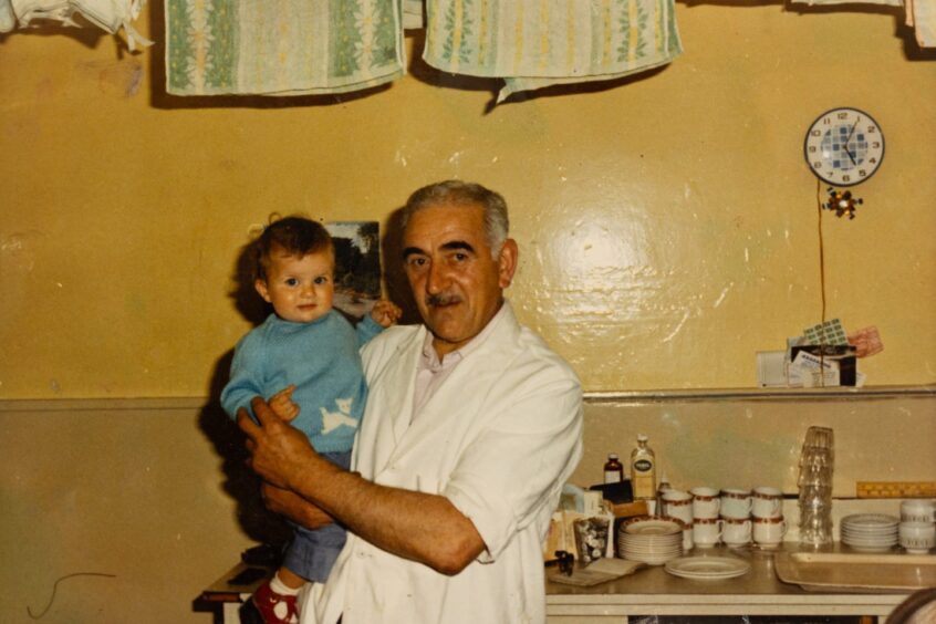 Photo of older man holding baby in Auchterarder chip shop in 1970s