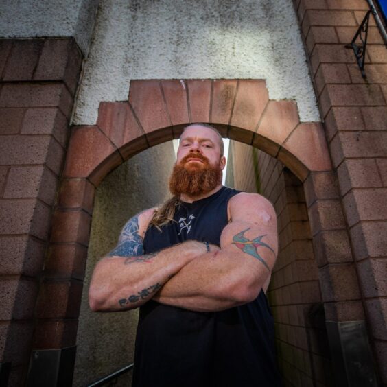 John Beattie, arms folded, with long red beard and hair and tattooed arms