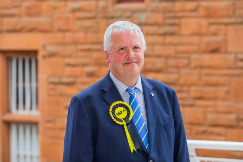 Councillor Eric Drysdale in suit wearing yellow SNP rosette