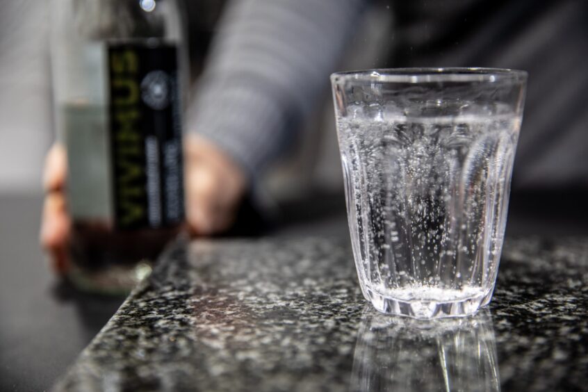 A glass of Vivimus sparkling water on a dark marble counter. 