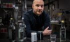 Vivimus Water founder Darren Peattie leaning on a counter in his factory with cans and bottles of his water.