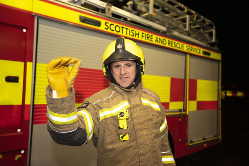 Dundee firefighter Alan Soutar stands in front of a fire engine in his work gear and pretends to throw a dart