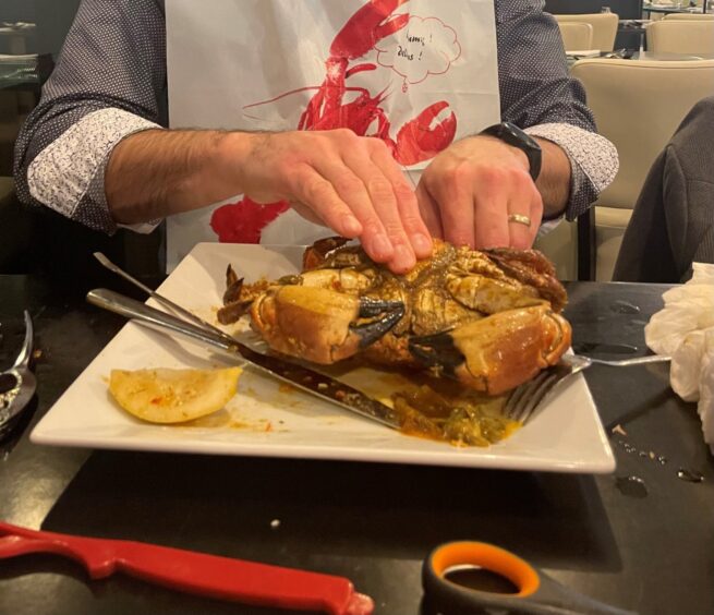 A man taking a cooked crab apart with his hands.