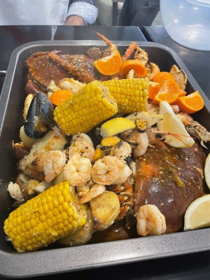 Surf and Turf's Boil in the Bag dish with two large crabs, prawns, corn of the cobs, oranges and more in a large oven tray.