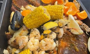 Surf and Turf's Boil in the Bag dish with two large crabs, prawns, corn of the cobs, oranges and more in a large oven tray.