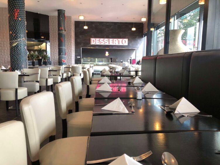 The interior of Surf and Turf restaurant has bornw tables, white chairs and a pink and white sign at the end for the desserts counter.