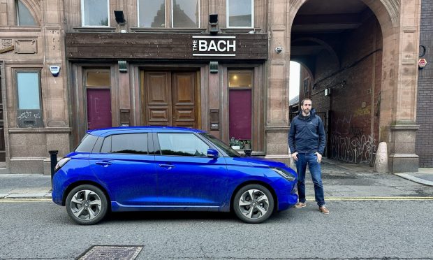 Motoring writer Jack McKeown beside a blue Suzuki Swift parked on a city street