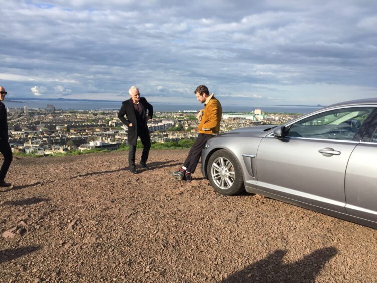 The actors during filming at the top of a hill in Edinburgh, with the city in the background