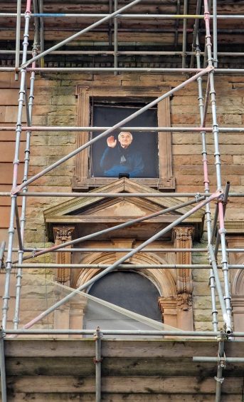 Life sized photo of actor Denis Lawson waving from window of hotel covered in scaffolding