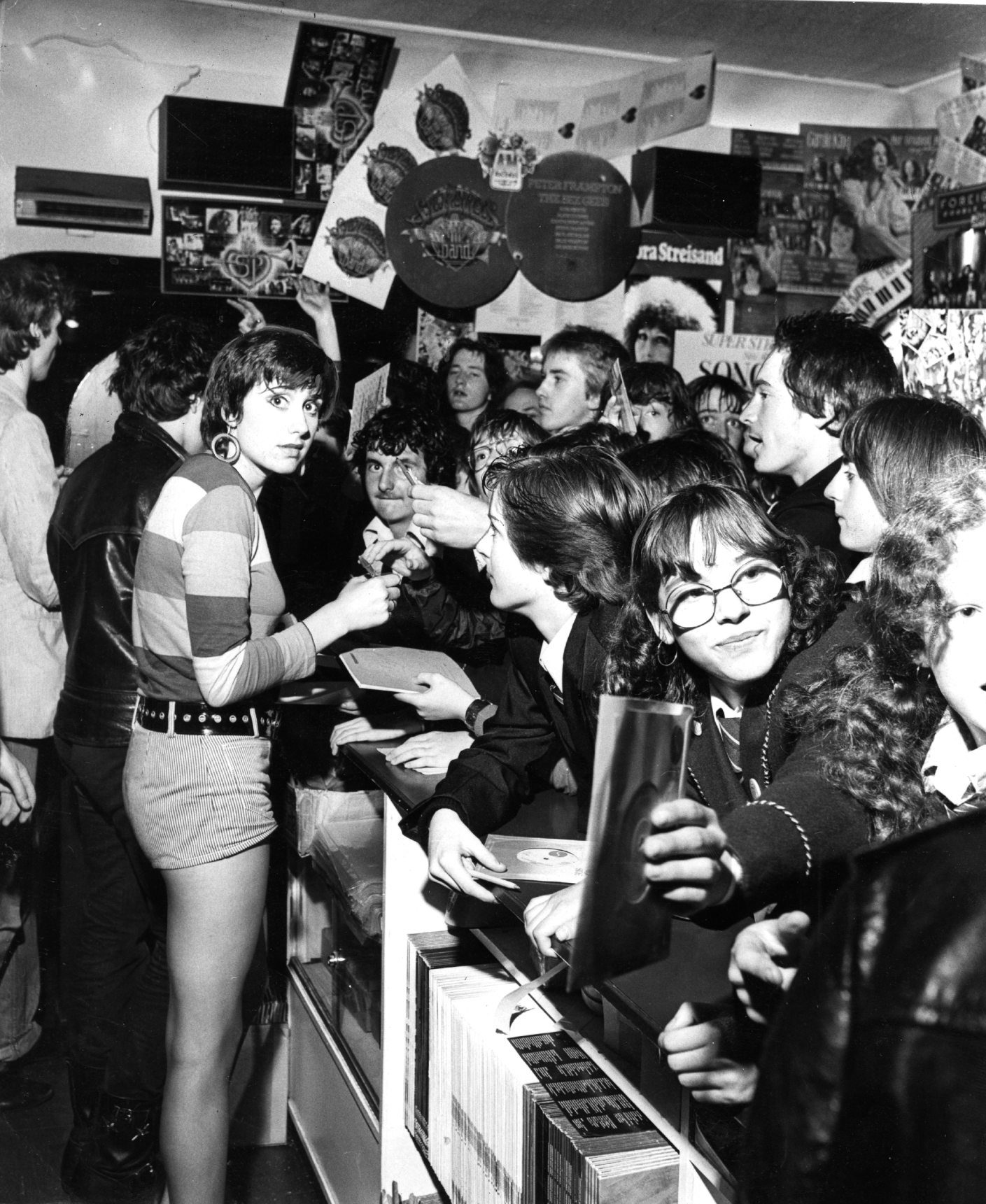 People leaning on the counter as The Rezillos singer Fay Fife signs autographs at Bruce's in August 1978. 