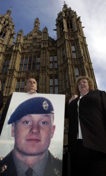 Jim and Yvonne Collinson holding large photo of their son outside Houses of parliament