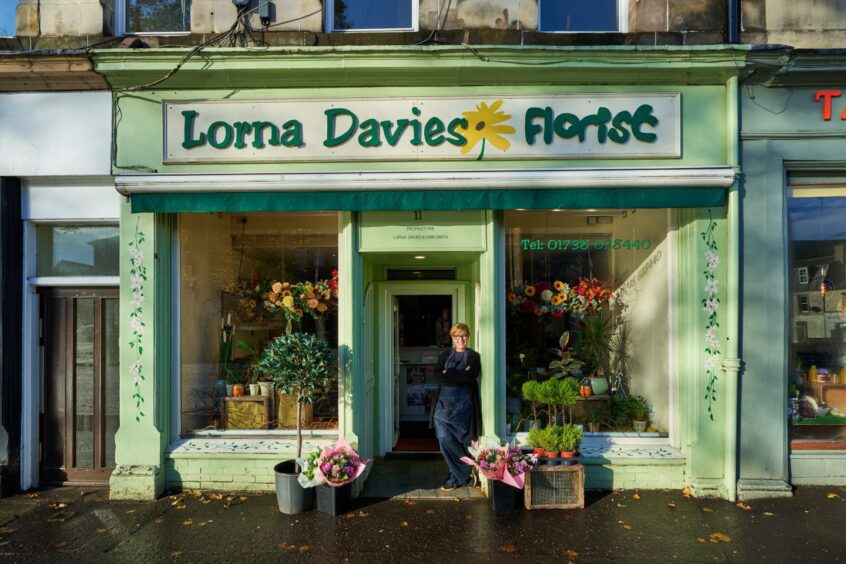 woman stands outside the facade of the Lorna Davies Florist shop in Perth