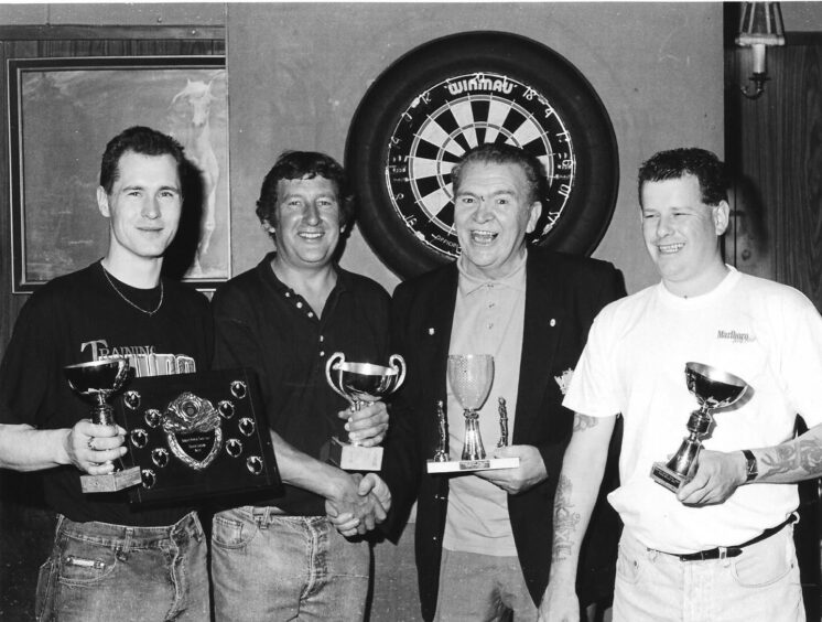 Arbroath Darts Summer League Trophy winners Peter Anderson, Geoff McGuigan, Willie Wales and Angus Cossans. smile with their trophies in front of a dart board