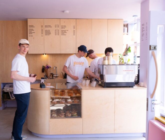 The interior of EH9 cafe has lilac walls and light pine coloured counters. There are a group of 4 people working at the counter in the photo.