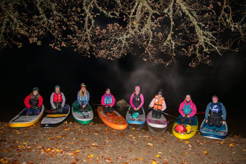 The group of female paddleboarders kneel on their boards at the shore of Loch Fascally at the end of the night-time paddle.