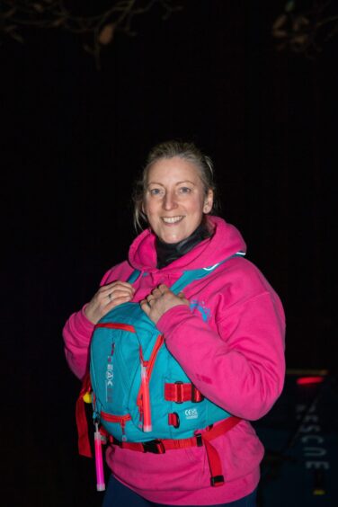 Lucy Mason, who runs Adventure paddleboarding poses in the darkness by Loch Fascally. She wears a bright pink hoodie over her wetsuit and a light blue life jacket.