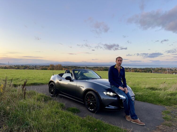 motoring writer Jack McKeown leans against the car's bonnet with a field in the background