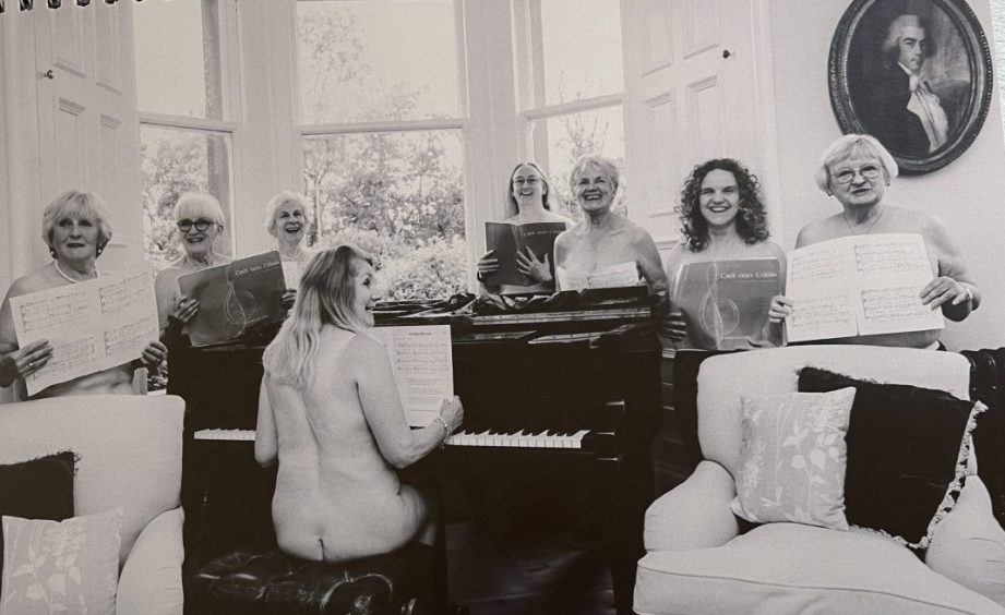 Topless women holding sheet music behind a piano