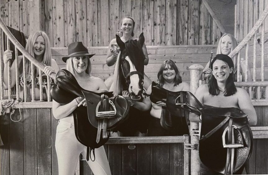 Group of topless women holding saddles in a stable