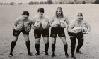 Black and white photo of topless women holding rugby balls at chest height