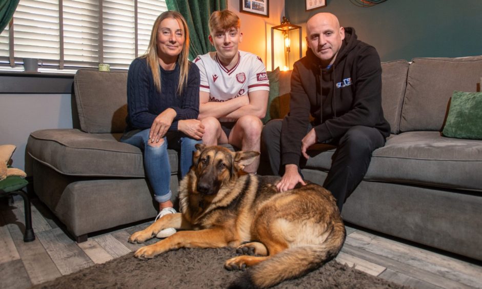 Guide dog puppy Craigie from Arbroath sitting at feet of his trainers 