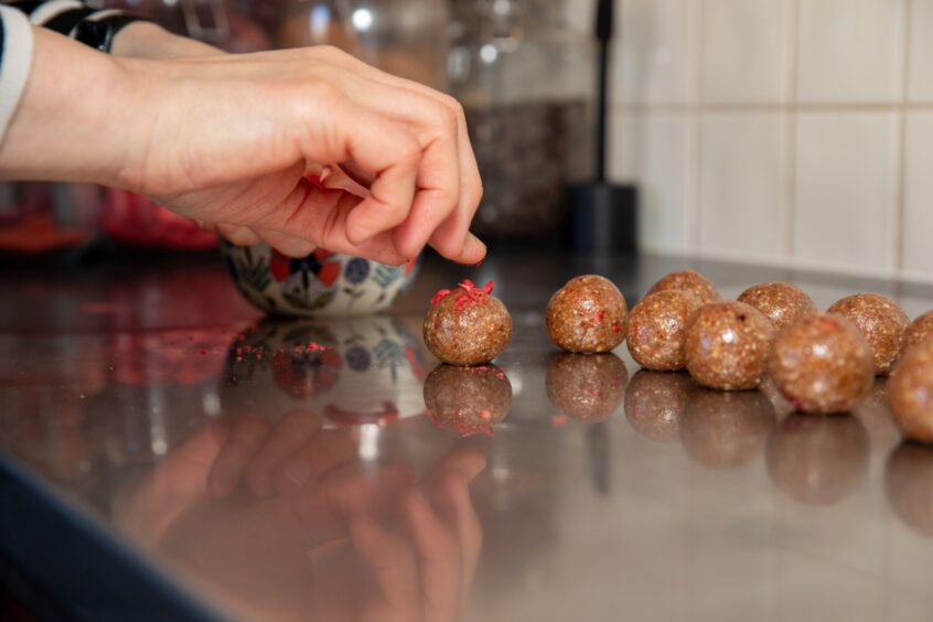 A hand coming donw to pick up a strawberries and cream Bliss Bites ball.