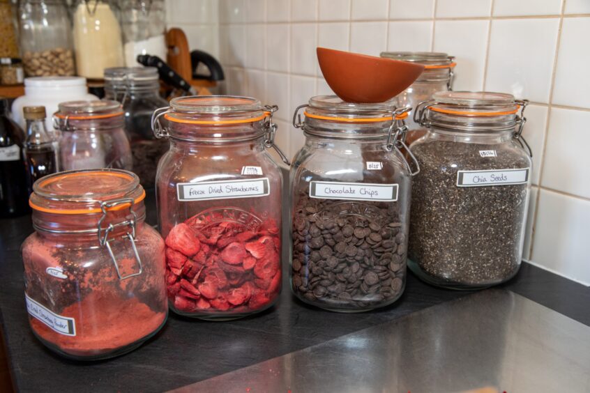 A row of large jars containing ingredients for Staci Clarke to make her Bliss Balls - including freeze-dried strawberries and chocolate chips.