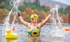 Image shows: a woman Stephanie Scott in a bright floral swimsuit swimming in a loch in the autumn. She is wearing a floral swimming hat on her head and black gloves. She is splashing the water with both hands.