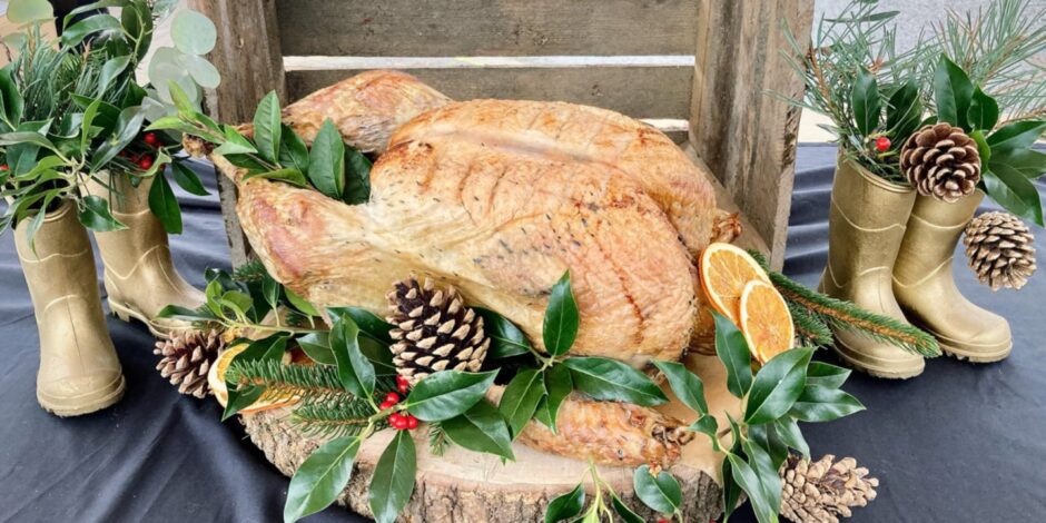 A cooked turkey decorated with fir cones and festive foliage and stuffed with an orange.