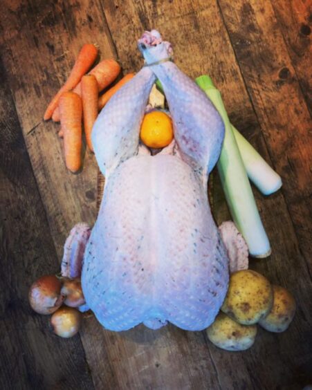 A whole raw turkey surrounded by raw veg on a wooden table.