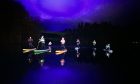 A group of 8 colourful paddleboraders in the dark on loch Fascally with a purple-tinged sky.