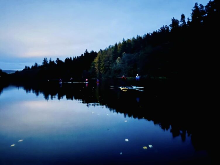 Paddleboarding progress along Loch Fascally as twilight sets in and the water reflects the darkening sky with a blue-ish hue.