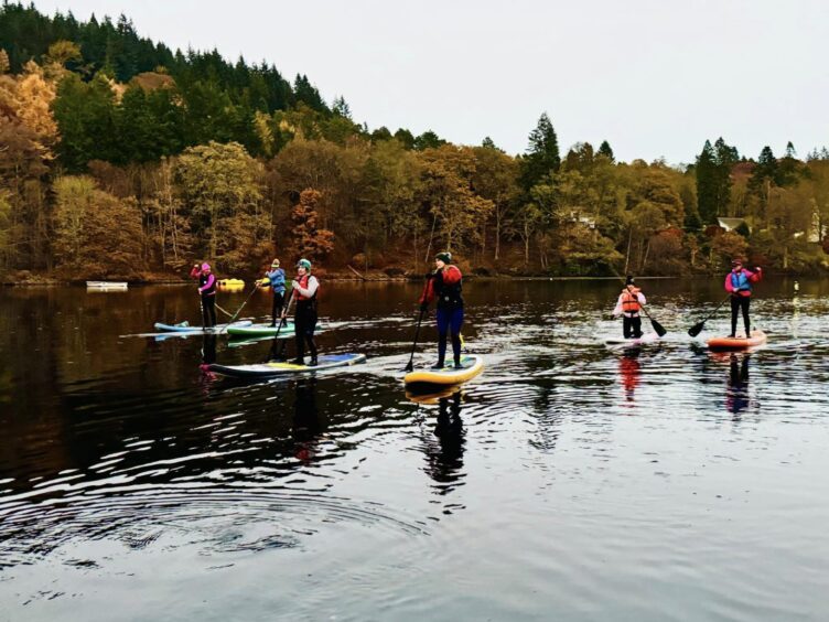 A group fo colourful paddleboarders setting off on Loch Fascally at dusk.