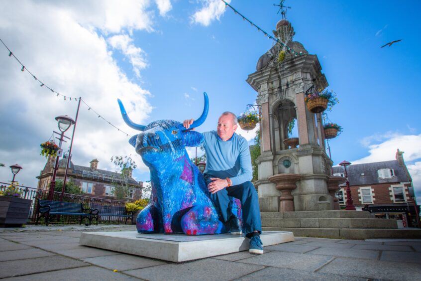 David McCann kneeling next to colourful cow sculpture