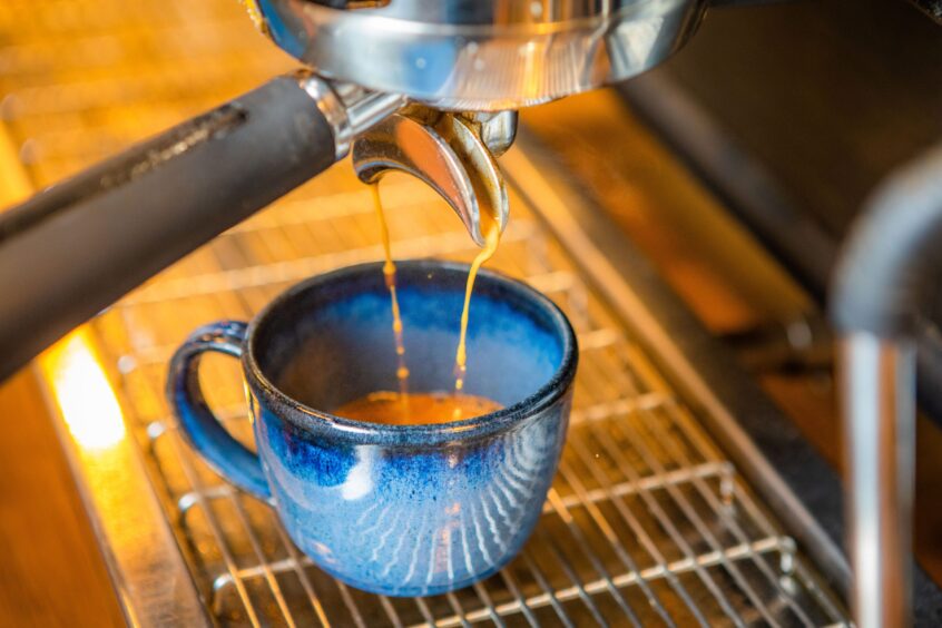 A cup of coffee being poured from a coffee machine.