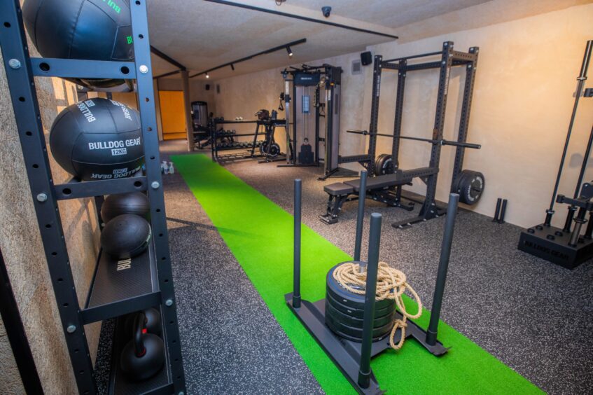 A green astro track on the gym floor with a weighted sled on it and gym benches at the sides.