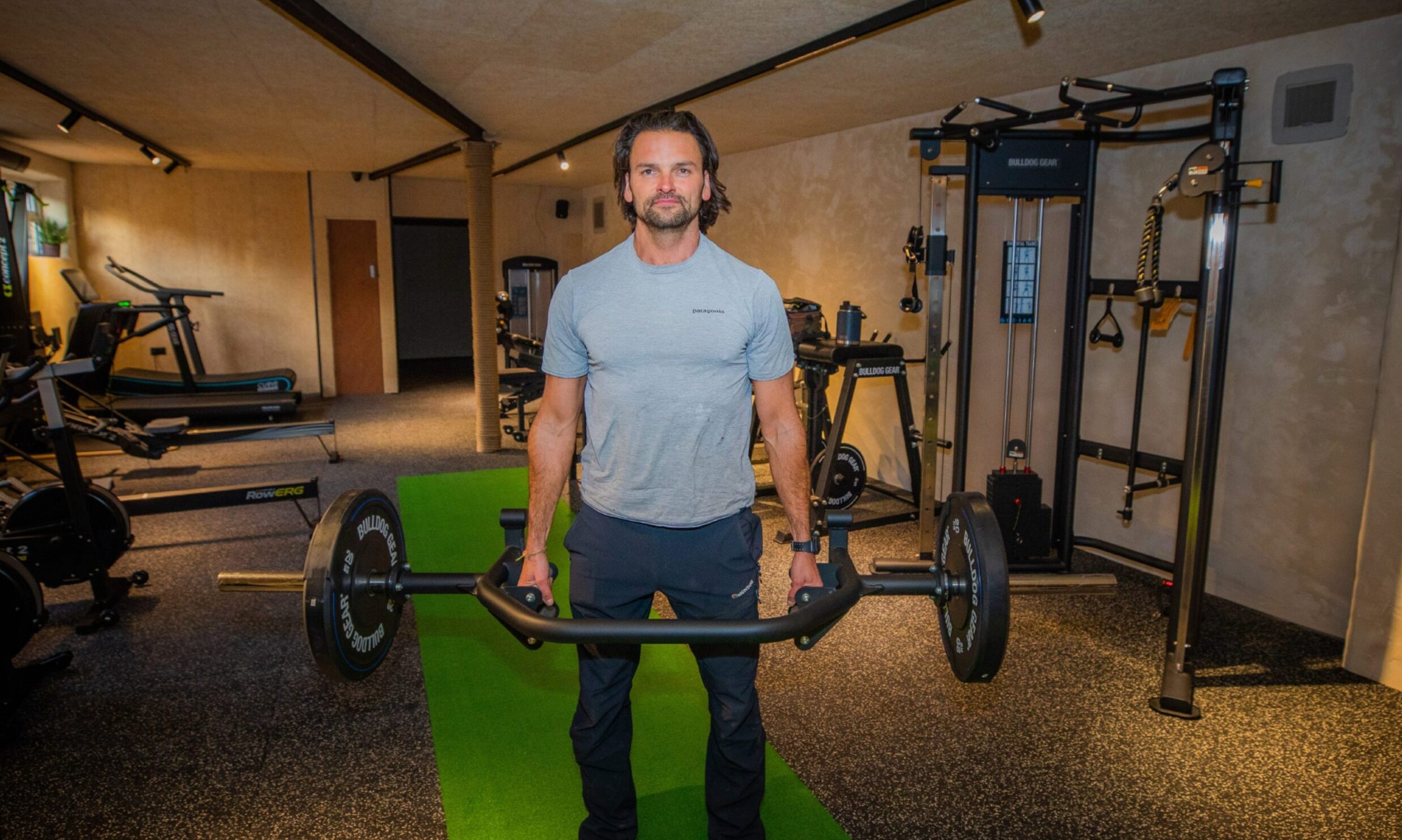 Simon stands in his gym holding a deadlift bar.