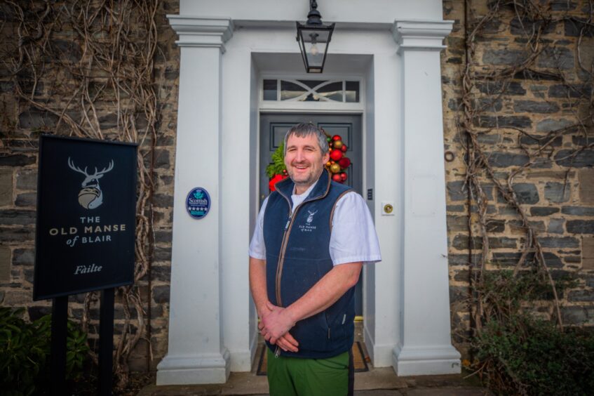 Chef Scott Davies stands outside The Old Manse of Blair's slate grey door which has a white surround and a red festive wreath,