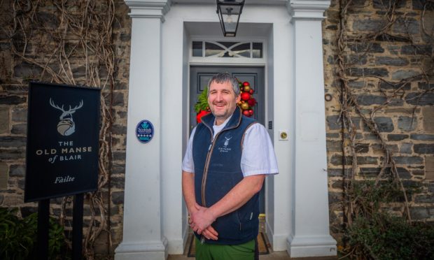 Chef Scott Davies stands outside The Old Manse of Blair's slate grey door which has a white surround and a red festive wreath,