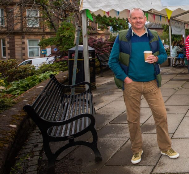 David McCann smiling holding disposable coffee cup in Crieff town square