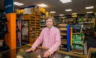 Betty Shakespeare behind counter at John Ferguson shop in Perth. Behind her are old fashioned wooden shelves full of clothing