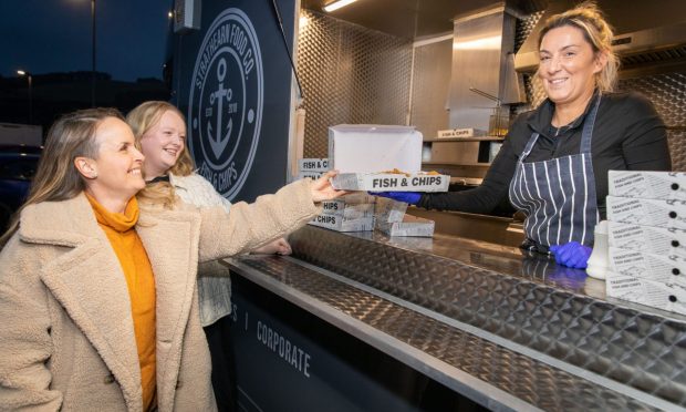 Rachel and Gee waiting outside the fish and chips van with Daniella holding out a fish supper form the van.